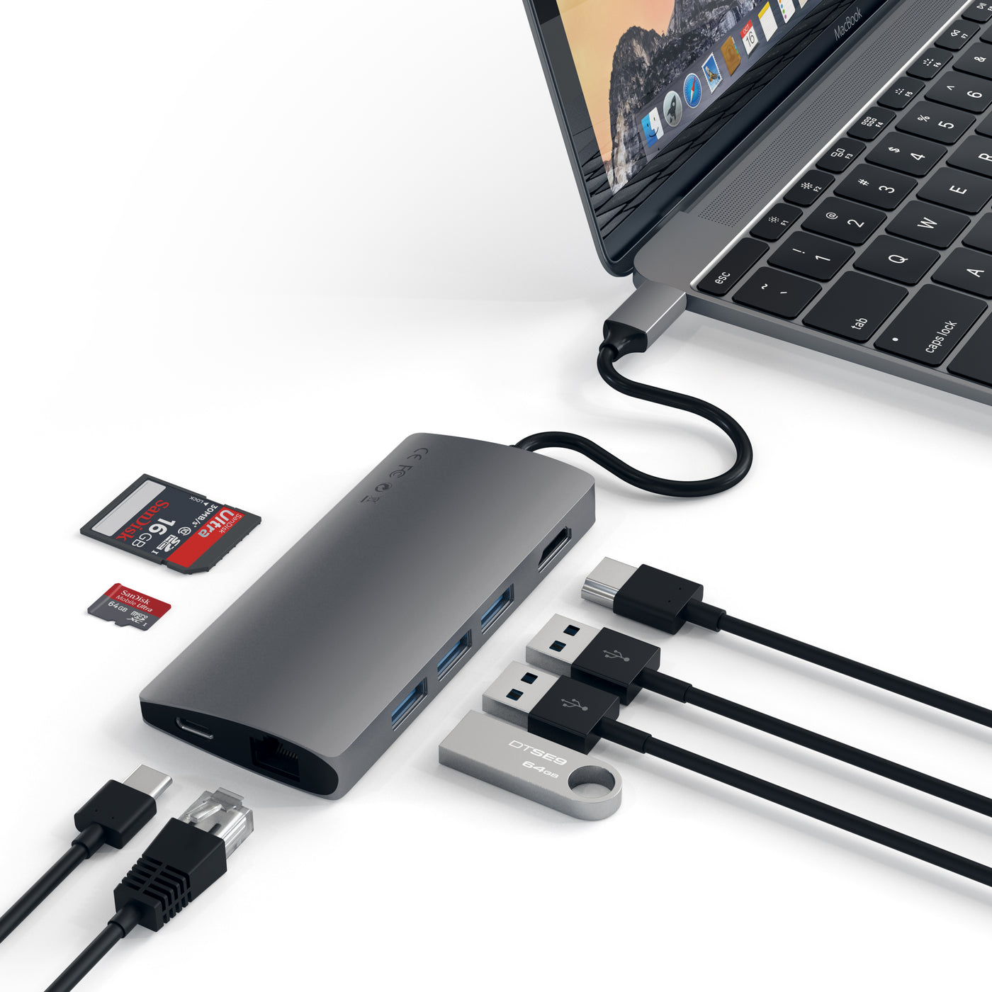 The Satechi Type-C Multi Port Adapter in Space Grey connected to a MacBook with 5 wires, 2 SD cards and 1 USB next to the ports of the adapter