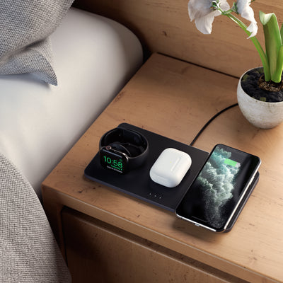 Top view of the Satechi Trio Wireless Charging Pad charging an Apple watch, AirPods and iPhone all at once on a light brown wooden bedside table